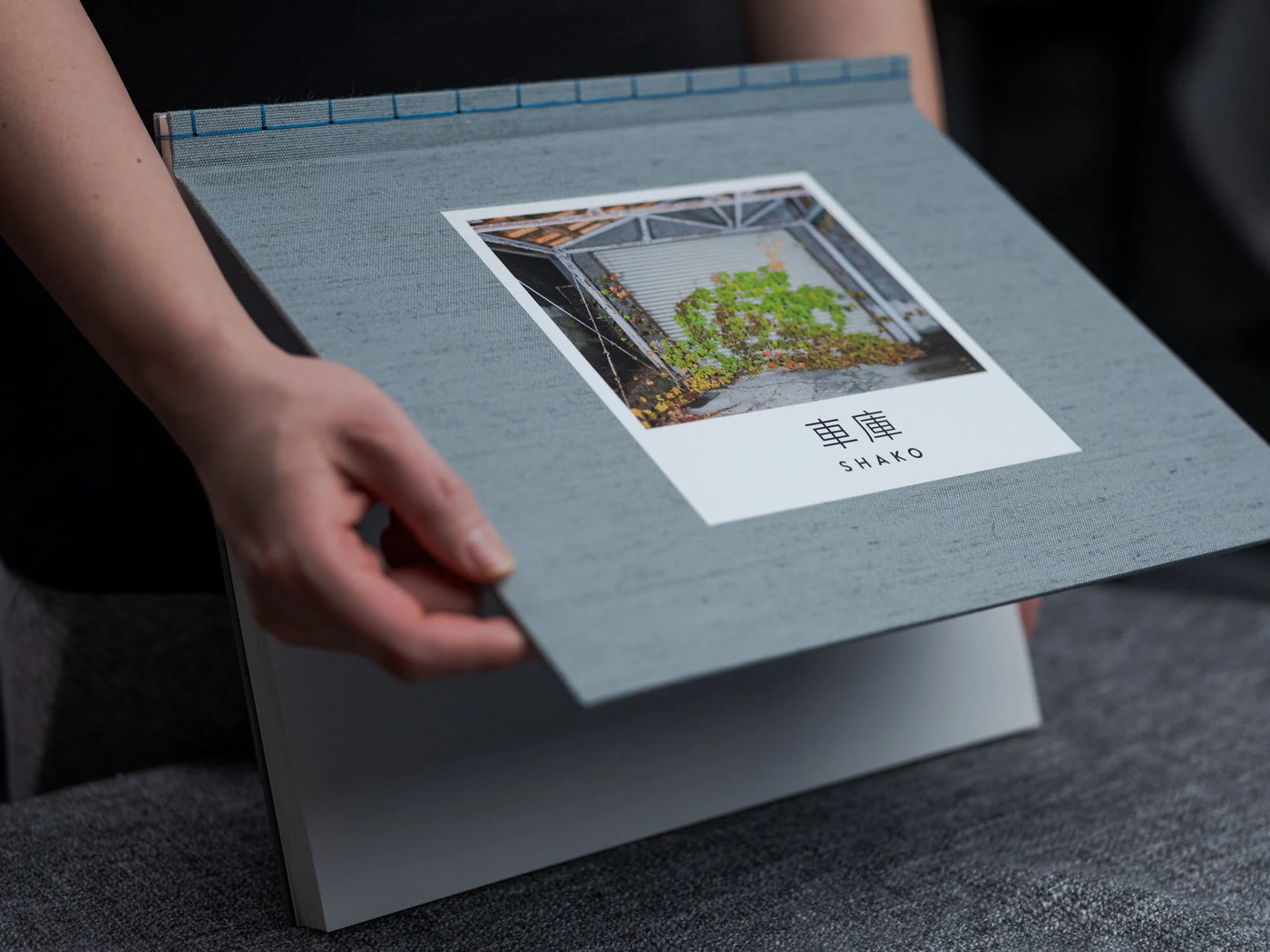 A hand lifting the cover of a cloth-bound photo book with a photograph tipped in on it